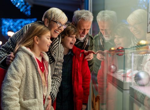 Happy grandparents with grandchildren looking at store window. An elderly man and woman are taking their grandchildren Christmas shopping.