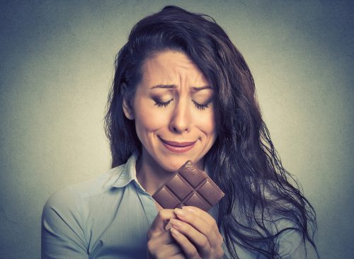 Portrait sad young woman tired of diet restrictions craving sweets chocolate isolated on gray wall background. Human face expression emotion. Nutrition concept. Feelings of guilt