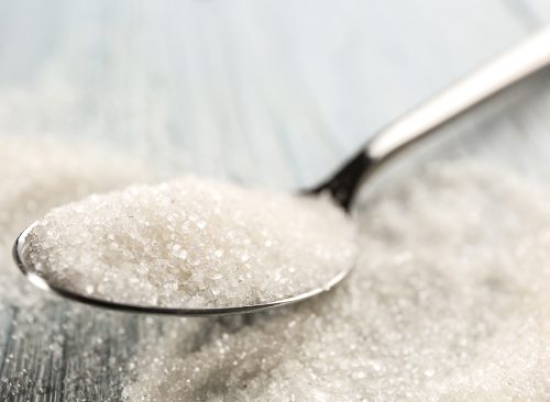Spoon with sugar on table, closeup