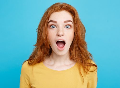 Close up Portrait young beautiful attractive redhair girl shocking with something. Blue Pastel Background. Copy space.