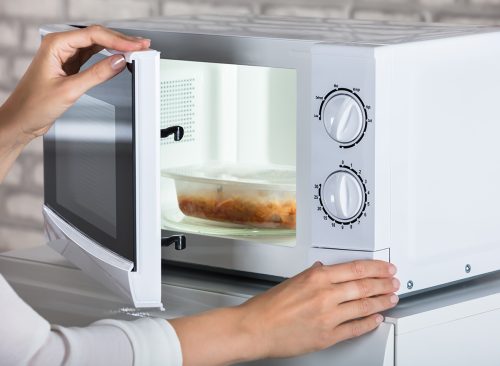 Woman's Hands Closing Microwave Oven Door And Preparing Food At Home