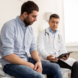 medicine, healthcare and people concept - doctor with clipboard and young male patient having health problem meeting at hospital
