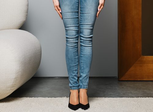 Cropped image of female legs in beige pantyhose and denim jeans standing straight