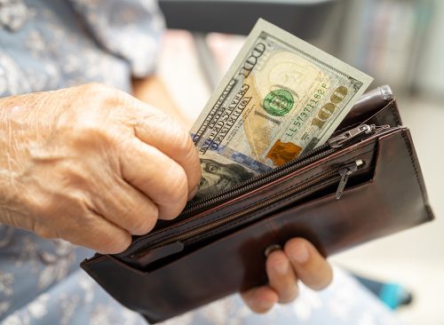 Asian senior woman holding and counting US dollar banknotes money in purse. Poverty, saving problem in retirement.