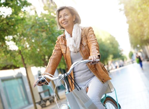 Senior woman riding city bike in town, wearing a leather jacket. 